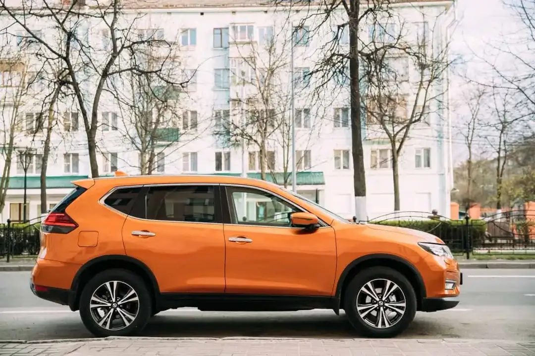 Pomarańczowy SUV do 50 tys. zaparkowany na tle białego budynku i drzew.