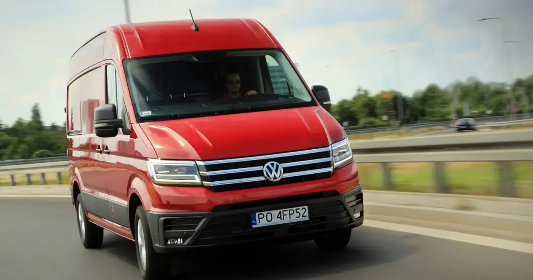 Czerwony VW Crafter pędzi autostradą. Kierowca w okularach prowadzi auto, które jest w ruchu.