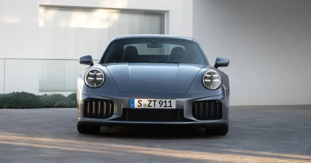 Szary Porsche 911 Turbo S z charakterystycznymi okrągłymi światłami i masywnym grillem, gotowy do jazdy.