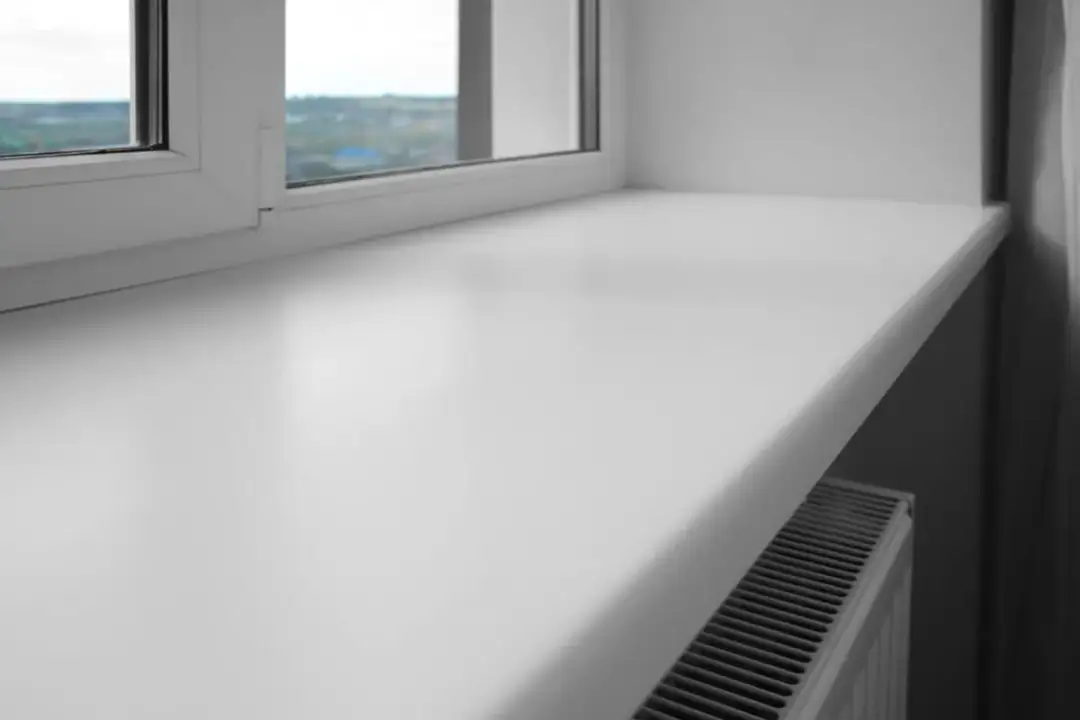 Biały, szeroki parapet okienny z tworzywa sztucznego, pod którym widać grzejnik. Czy parapet jest konieczny? To pytanie zadaje sobie wielu, ale ten dodaje funkcjonalności.