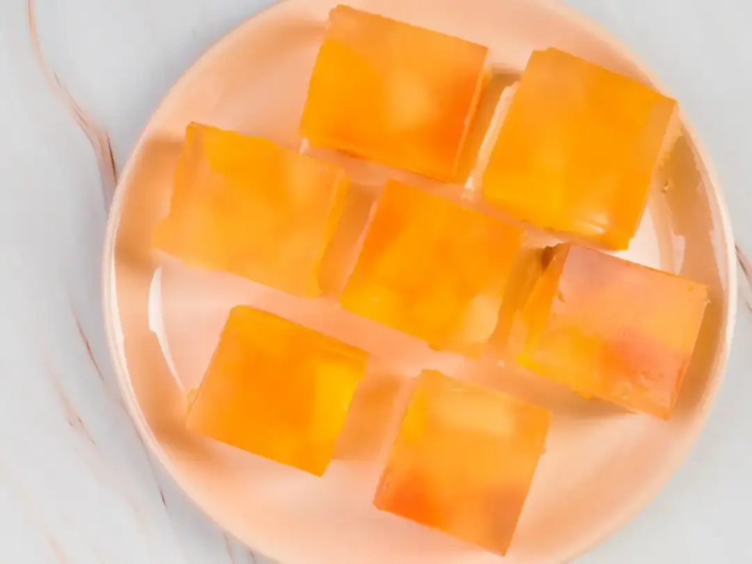 Siedem pomarańczowych kostek galaretki owocowej z kawałkami owoców. Czy galaretka owocowa jest zdrowa? To zależy od składników.