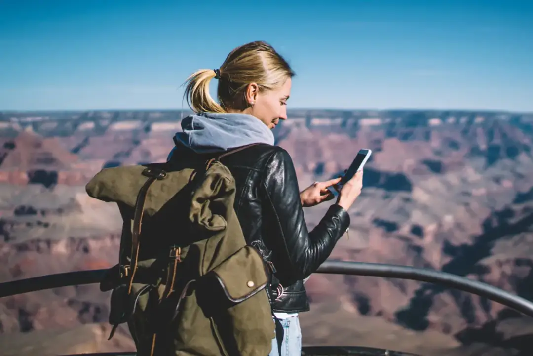 Kobieta z plecakiem sprawdza telefon, być może co to jest roaming danych, na tle Wielkiego Kanionu.