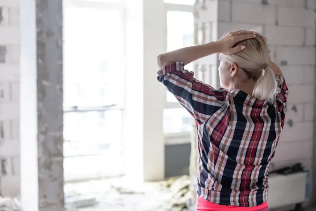 Kobieta z rękami na głowie w niedokończonym domu, zastanawia się, jak zbudować dom.
