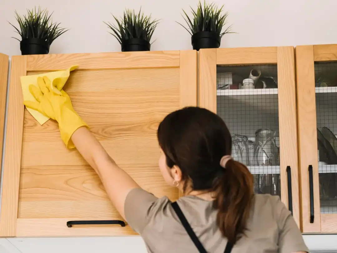 Kobieta w żółtej rękawiczce czyści drewnianą szafkę kuchenną żółtą ściereczką.