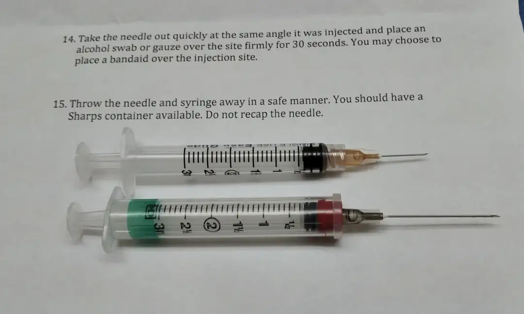 Dwie strzykawki z igłami, jedna z pomarańczową osłonką, druga z czerwoną. Pokazują, jaka igła do zastrzyku domięśniowego.