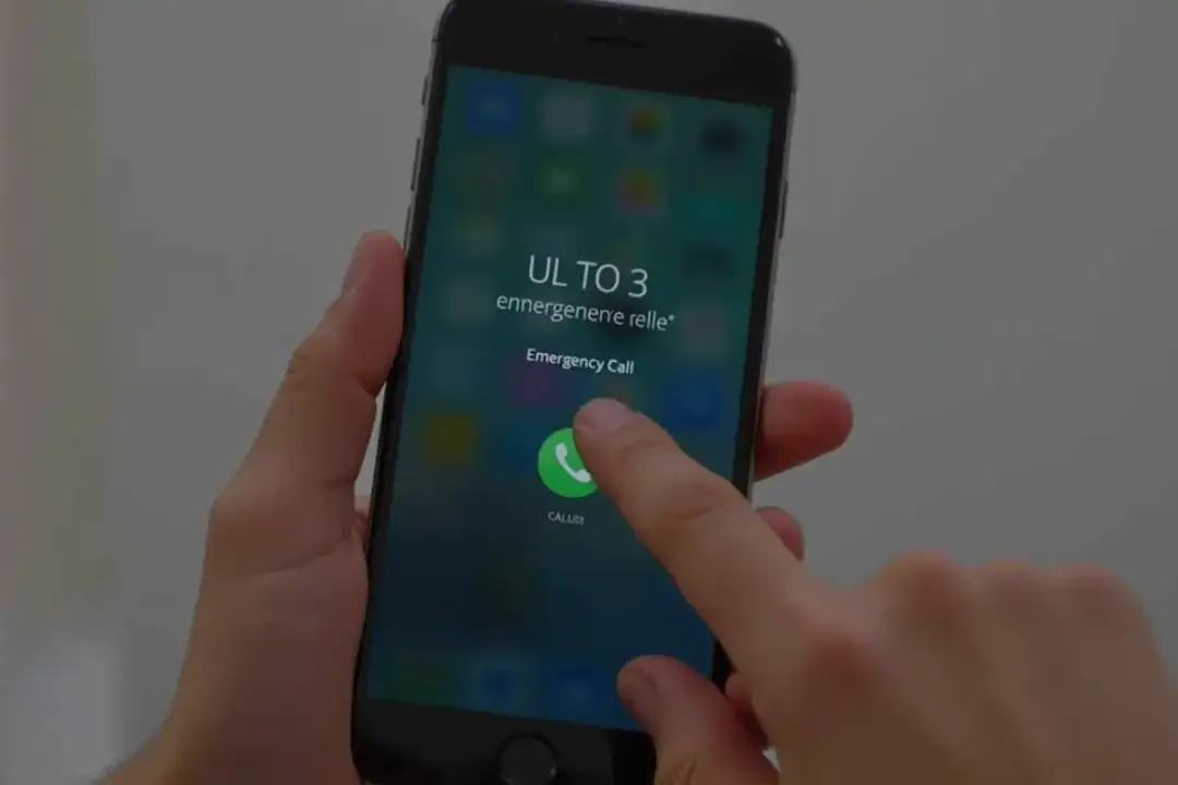 Dłoń trzyma smartfon z ekranem blokady i ikoną połączenia alarmowego.