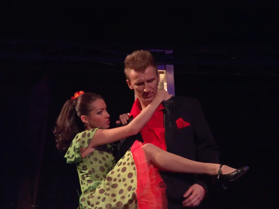 Tancerze w kostiumach z musicalu "Grease" w Warszawie. Ona w zielonej sukience w grochy, on w czarnej marynarce.