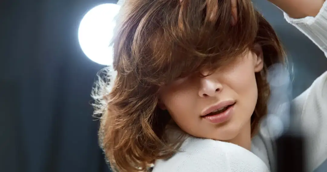 Kobieta z burzą brązowych włosów, zastanawiająca się, jak utrwalić fryzurę na wesele. Delikatne światło podkreśla jej urodę.