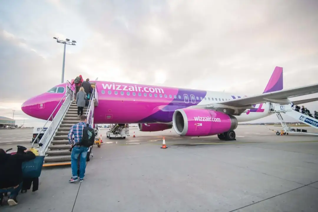 Różowy samolot Wizz Air z pasażerami wsiadającymi po schodkach na lotnisku.