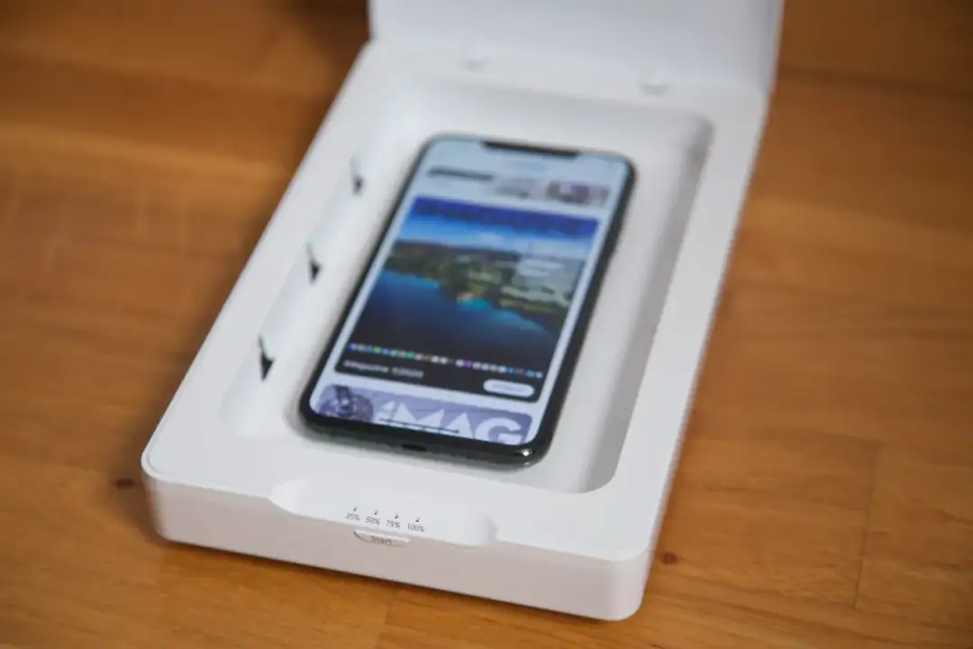 Czy odkażanie telefonu promieniami UV to skuteczna metoda na bakterie? Smartfon w białym pudełku z lampami UV, gotowy do dezynfekcji.