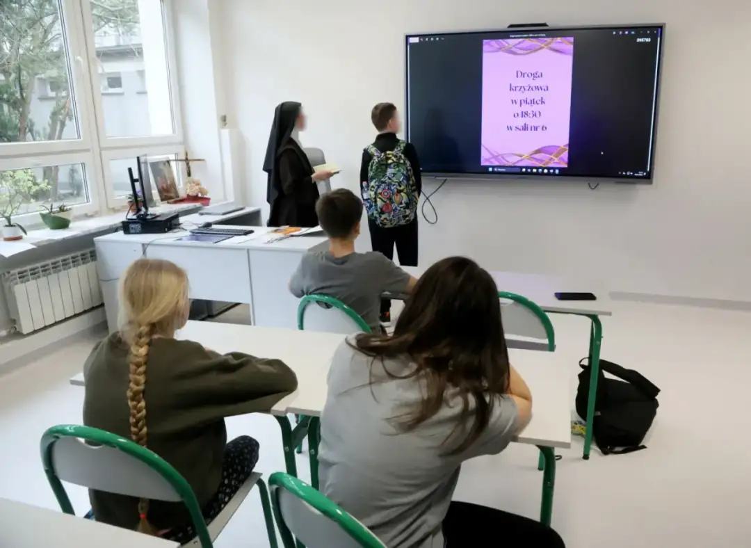 Nauczycielka w habicie i uczniowie patrzą na ekran z informacją o Drodze Krzyżowej. Czy religia liczy się do średniej?