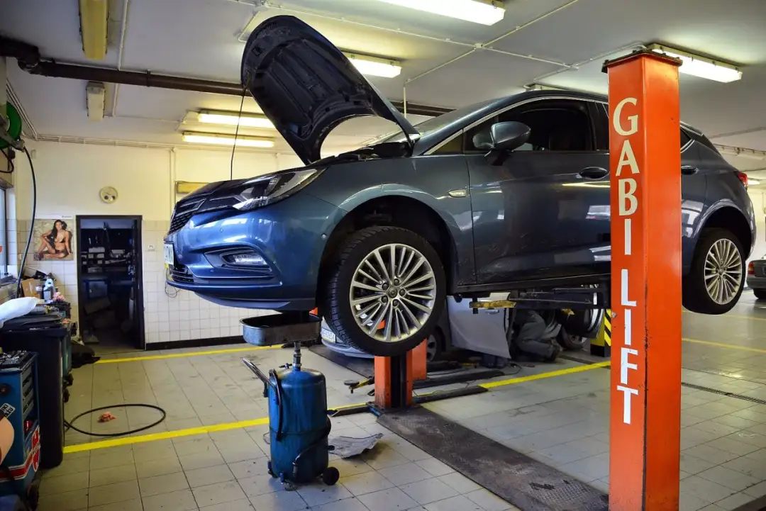 Samochód na podnośniku w warsztacie. Zastanawiasz się, ile kosztuje wymiana oleju w samochodzie? Tutaj dowiesz się, jak przebiega serwis.