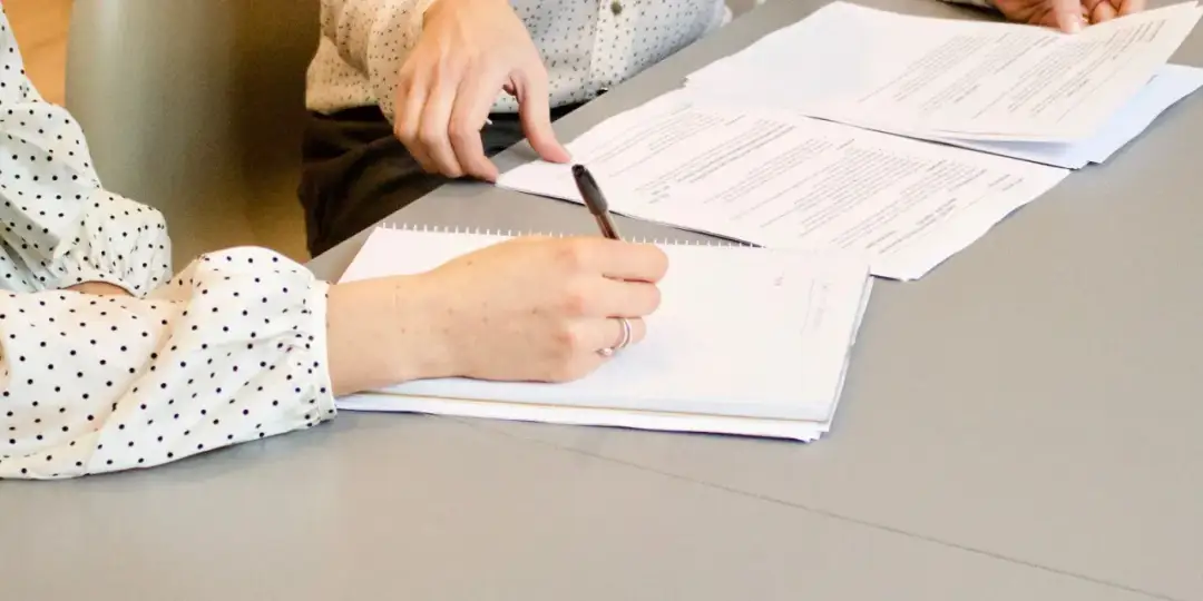 Dwie osoby przy stole analizują dokumenty. Jedna pisze w notatniku, druga wskazuje na papiery. To może być moment ustalania, jakie dokumenty do rozdzielności majątkowej są potrzebne.