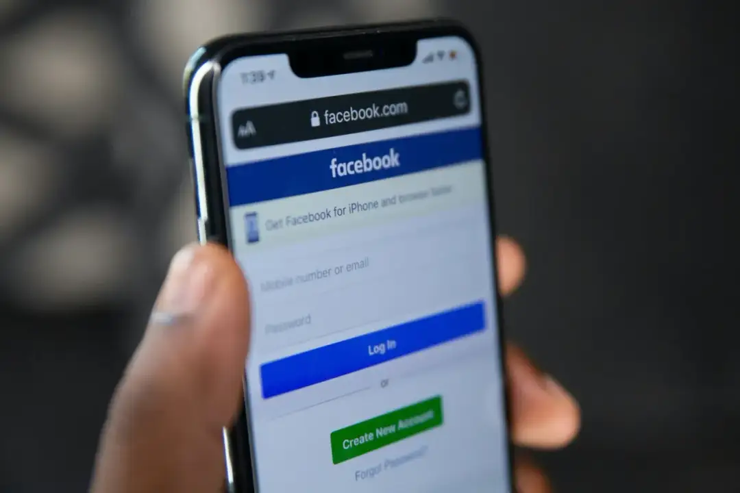 Dłoń trzyma smartfon z ekranem logowania Facebooka. Szukasz sposobu, jak odzyskać konto na FB bez maila i telefonu?