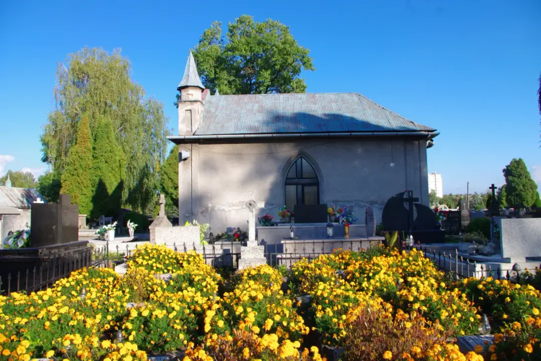 Cmentarz komunalny Oświęcim. Wśród żółtych kwiatów i zieleni widać kaplicę cmentarną i nagrobki.