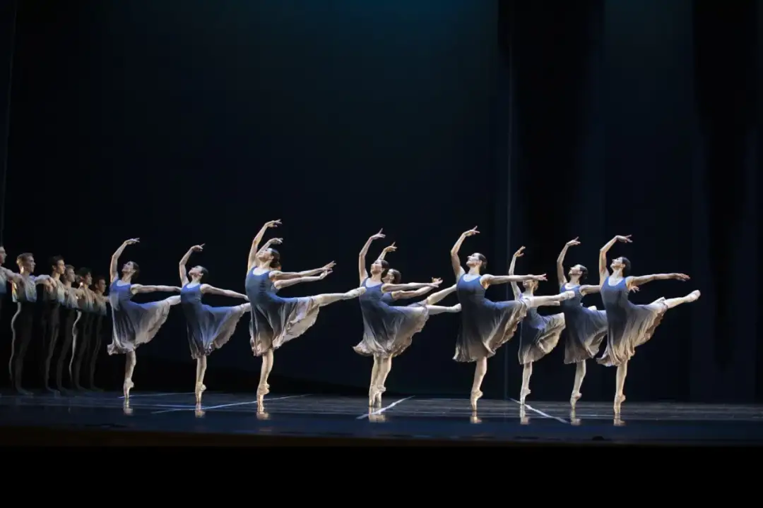 Tancerki w granatowych sukniach na scenie, prezentujące piękno baletu. Warszawa repertuar zachwyca.