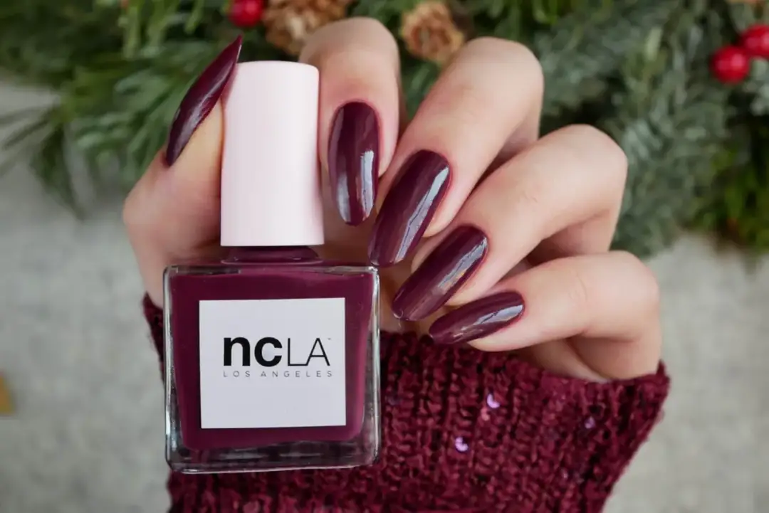 Dłonie z idealnym, bordowym manicurem prezentują buteleczkę lakieru NCLA. To jedne z najlepszych lakierów do paznokci, idealne na zimowe dni.