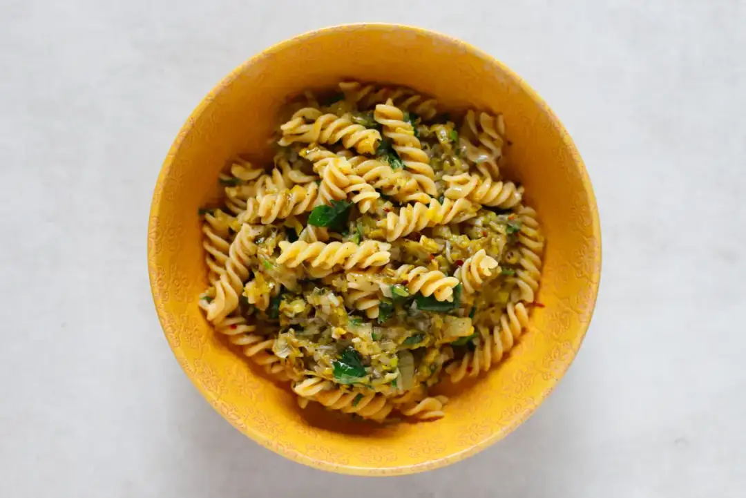 Fusilli z porem i zielonymi ziołami w żółtej misce. Pyszny makaron z porem, idealny na szybki obiad.