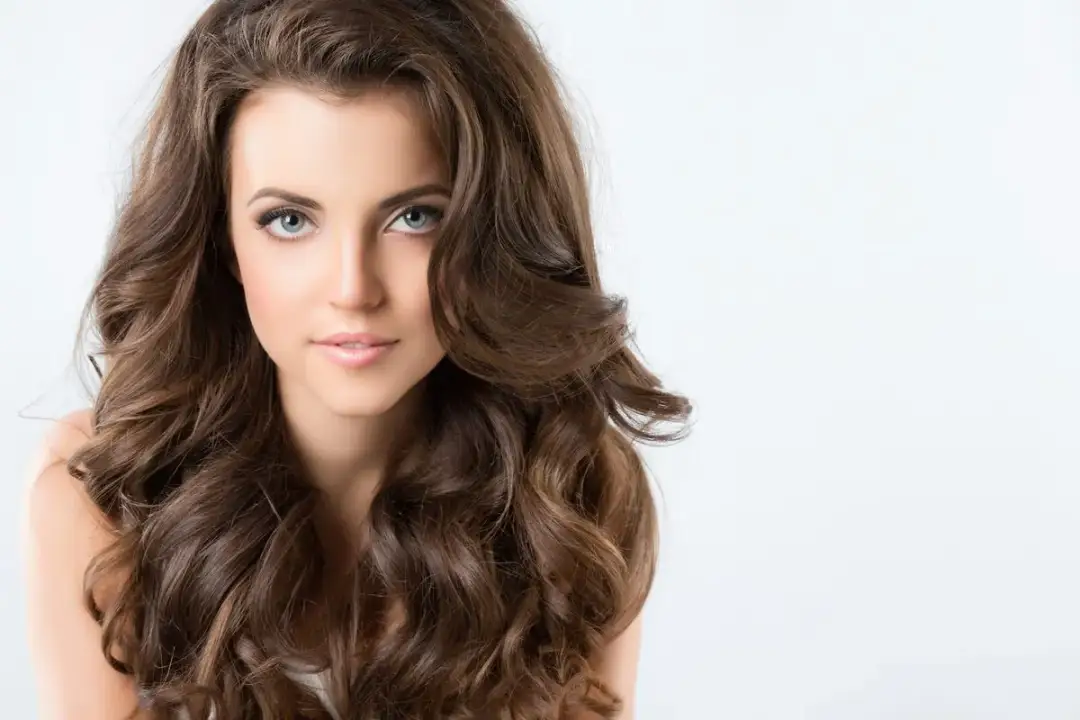 Piękna kobieta z falowanymi brązowymi włosami, idealna inspiracja do fryzury dla pociągłej twarzy. Galeria fryzur.