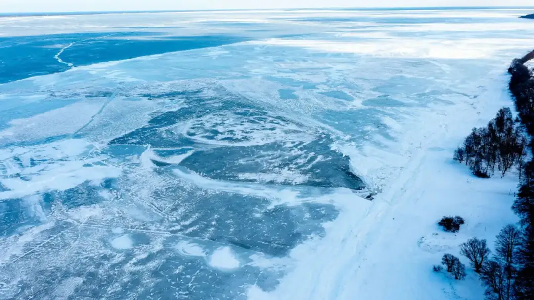 Zamarznięte morze bałtyckie, pokryte lodem i śniegiem, z widocznym brzegiem porośniętym drzewami.