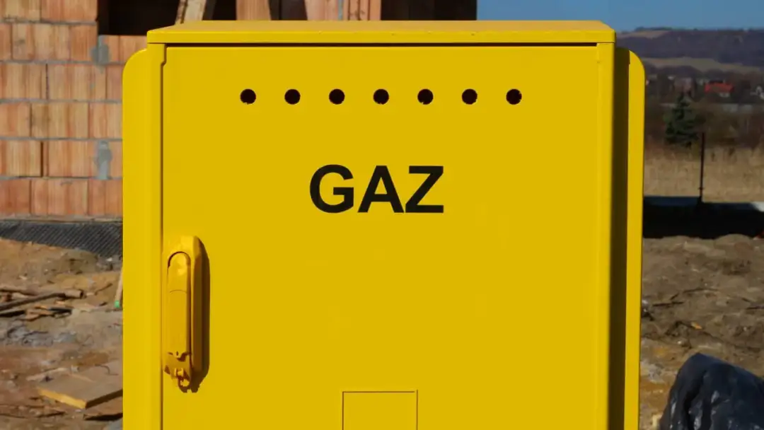 Żółta skrzynka gazowa z napisem "GAZ" na tle budowy.