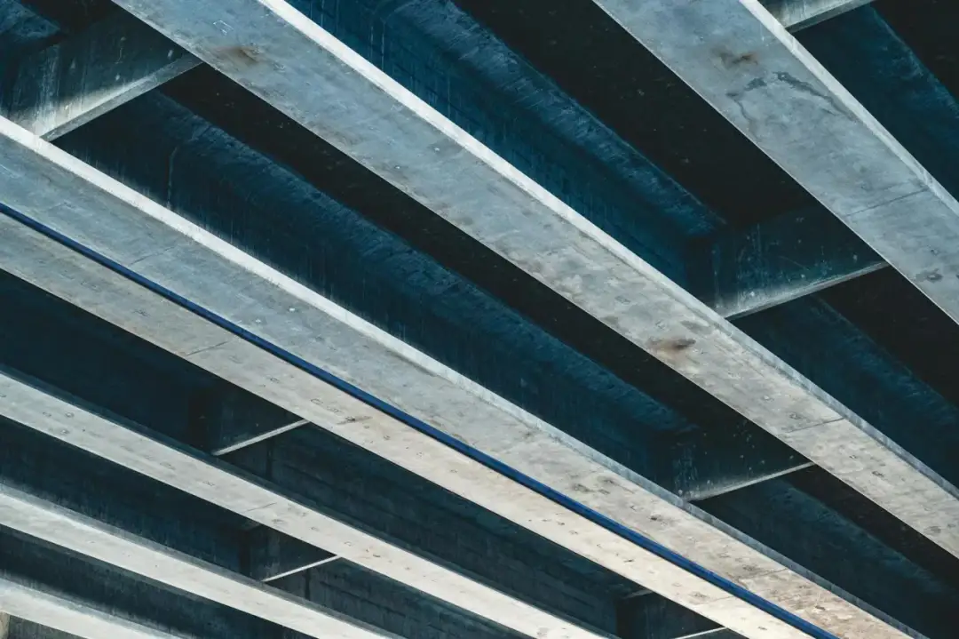 Betonowe belki stropowe ułożone pod kątem, tworzące cień i światło.