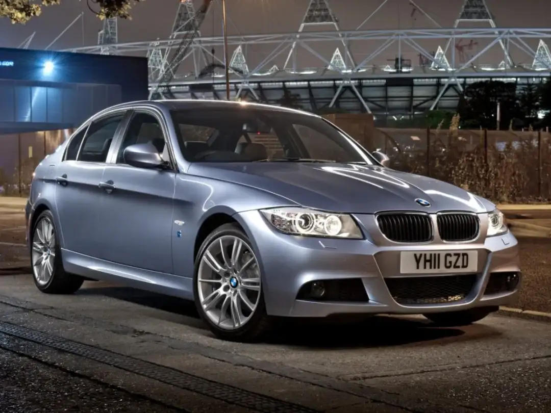 Srebrny sedan BMW E90 330d stoi na ulicy nocą, z tyłu widać stadion.