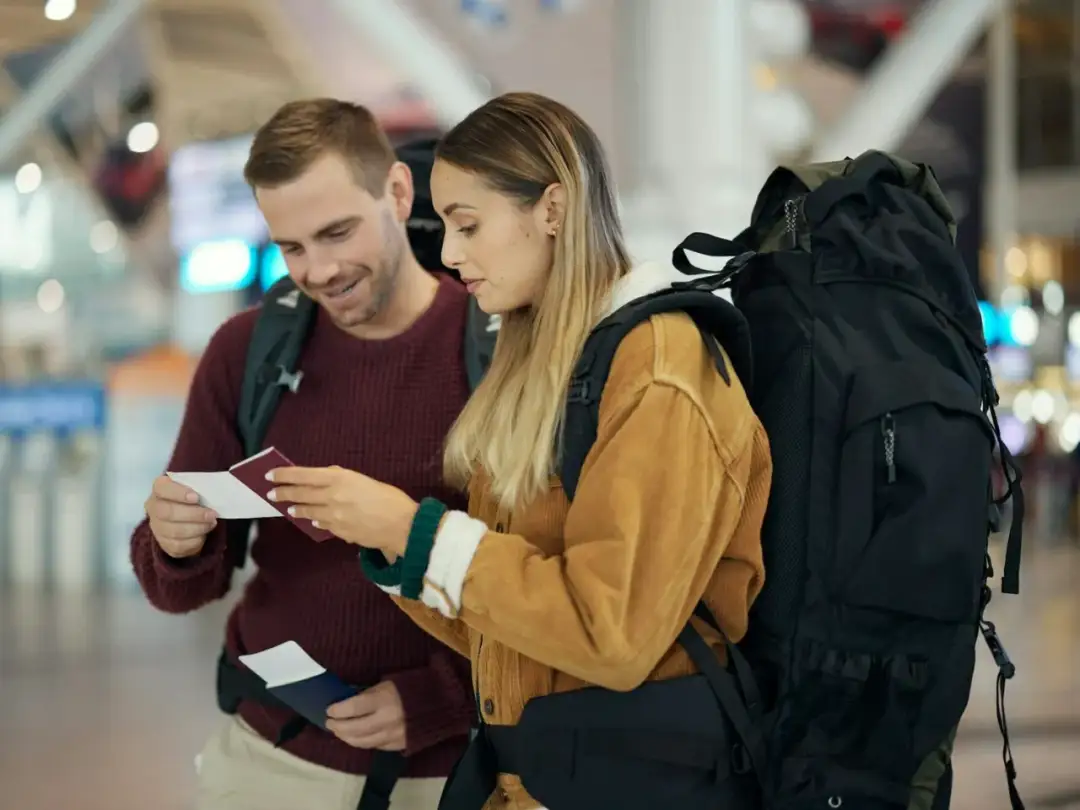Para podróżnych z plecakami przegląda paszporty i bilety w terminalu lotniczym.