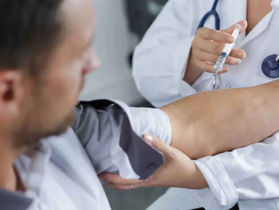 Lekarz podaje zastrzyk domięśniowy. Widoczne jest zgrubienie po zastrzyku na ramieniu pacjenta.