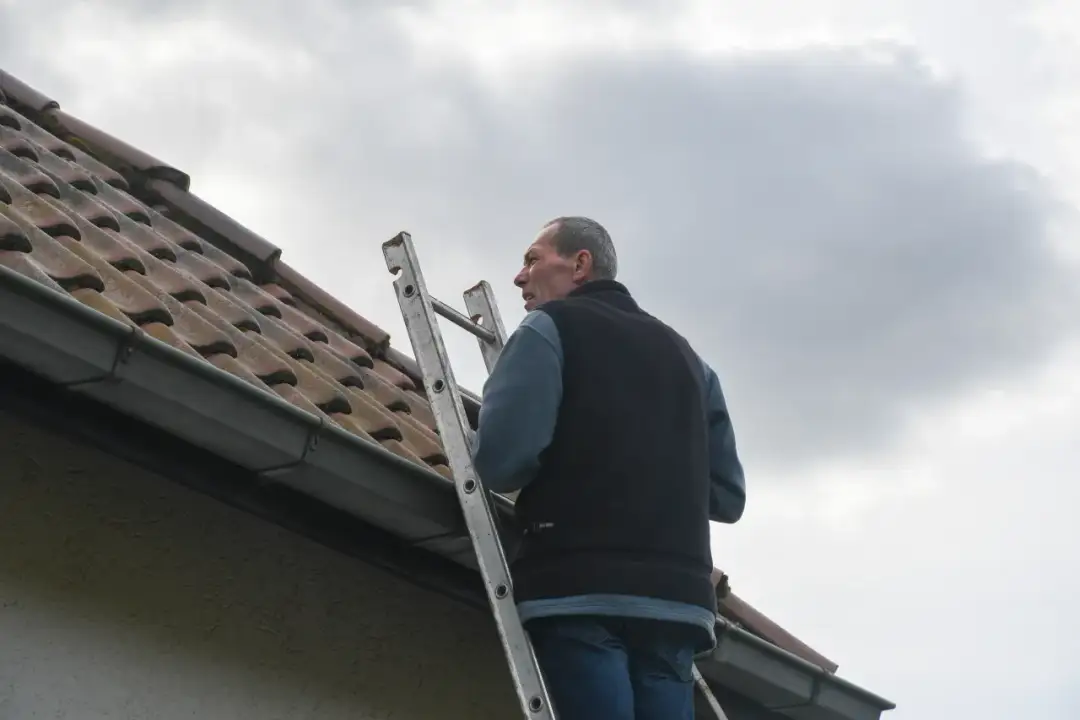 Mężczyzna na drabinie przy dachu. Jak obliczyć kąt nachylenia dachu jednospadowego?