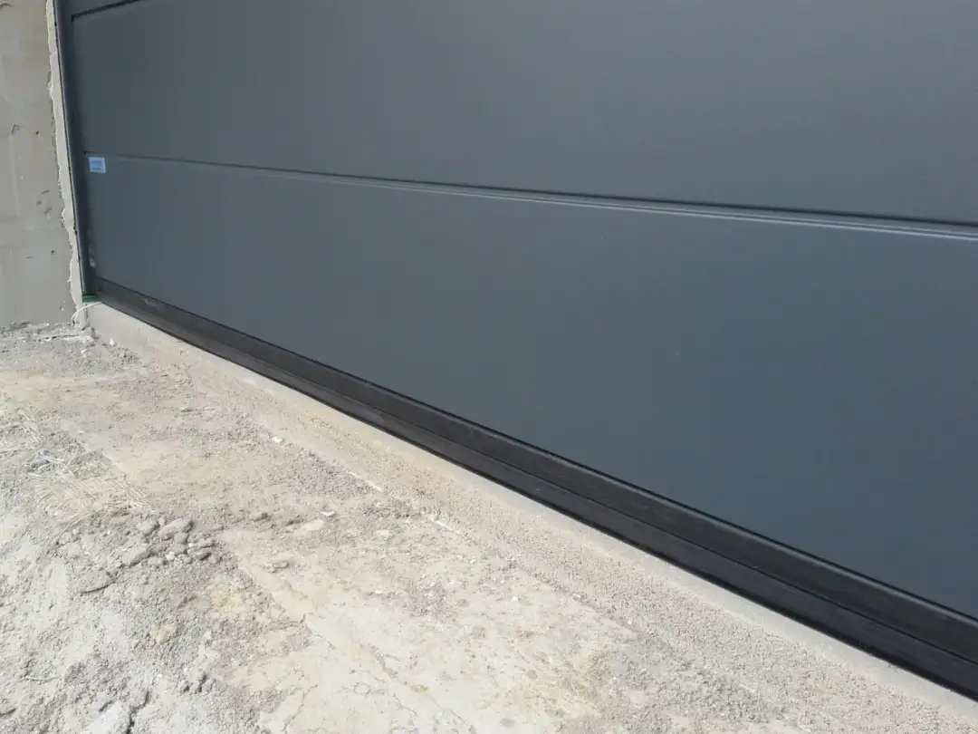 Szara brama garażowa z czarną uszczelką na dole. Dowiedz się, jak uszczelnić bramę garażową, by chronić przed zimnem i wilgocią.