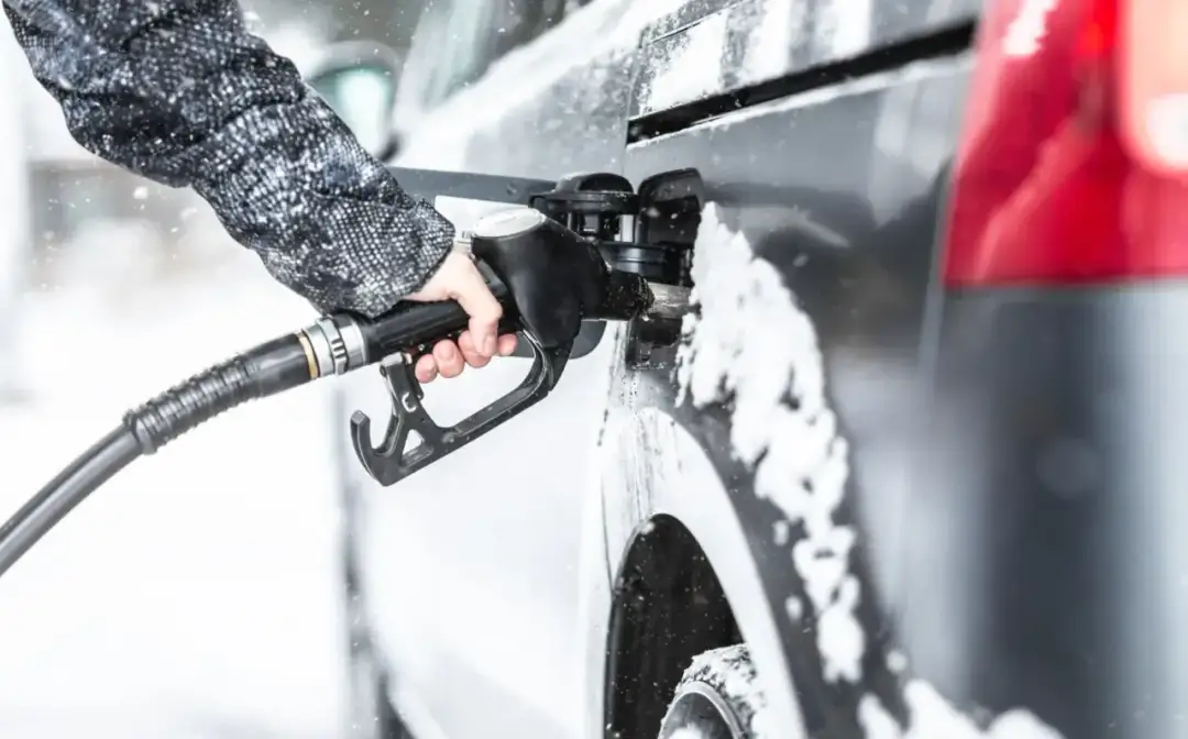 Dłoń trzymająca pistolet paliwowy przy samochodzie pokrytym śniegiem.