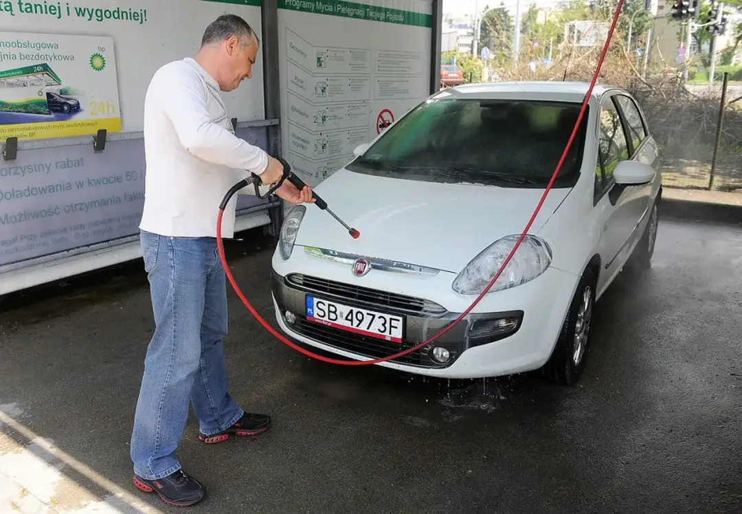 Mężczyzna myje białe auto na samoobsługowej myjni. Wygodna myjnia płatność kartą, szybkie i skuteczne czyszczenie.