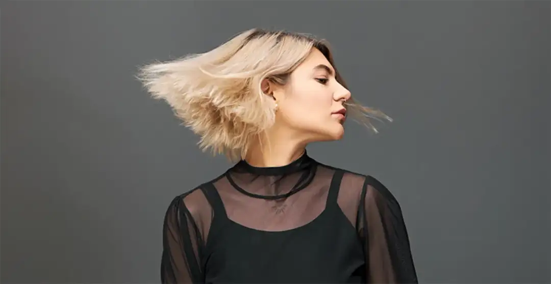 Kobieta z blond włosami w ruchu, w czarnej, prześwitującej bluzce. Efekty stylizacji fryzury.