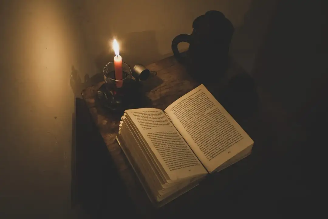 Światło świecy oświetla otwartą książkę, sugerując, jak literatura przedstawia kontrast między światem biedy a światem bogactwa.
