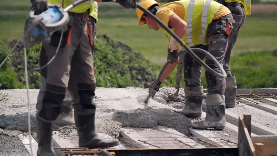 Budowlańcy w kamizelkach i kaskach wylewają beton na strop. Prawidłowe wykonanie to klucz do tego, jak dbać o świeży strop.