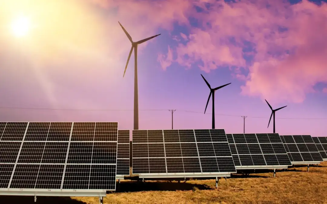 Panele słoneczne i wiatraki na tle zachodzącego słońca.