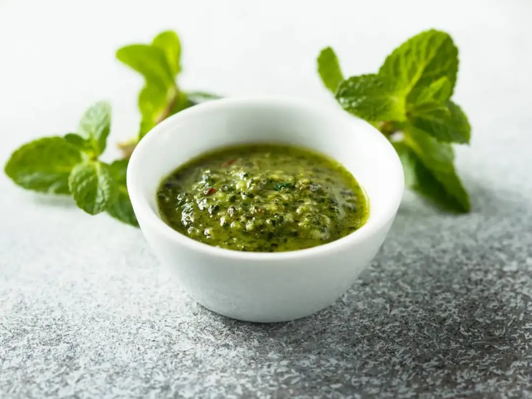 Zielony, orzeźwiający sos miętowy do kebaba, w białej miseczce, otoczony świeżymi listkami mięty.