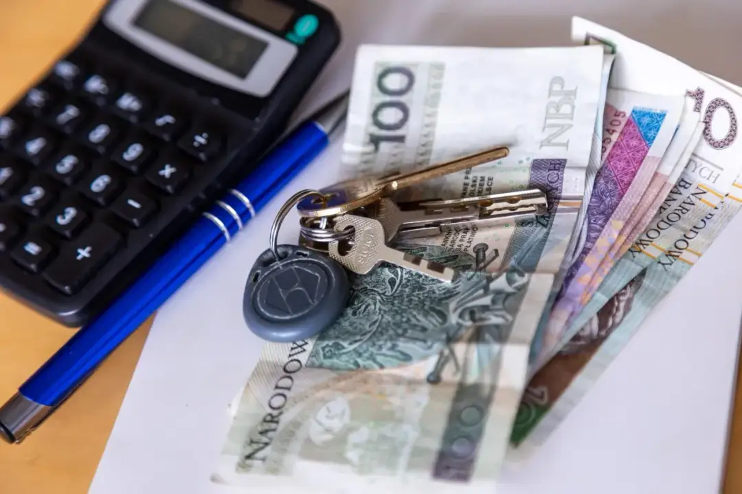 Klucze, pieniądze i kalkulator na biurku.