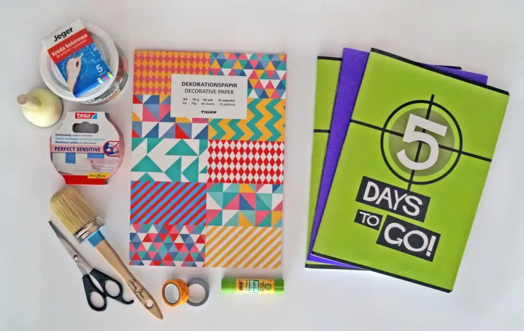 Materiały do kreatywnego ozdabiania zeszytów: kolorowy papier, taśmy, klej, nożyczki, pędzel i kredy.