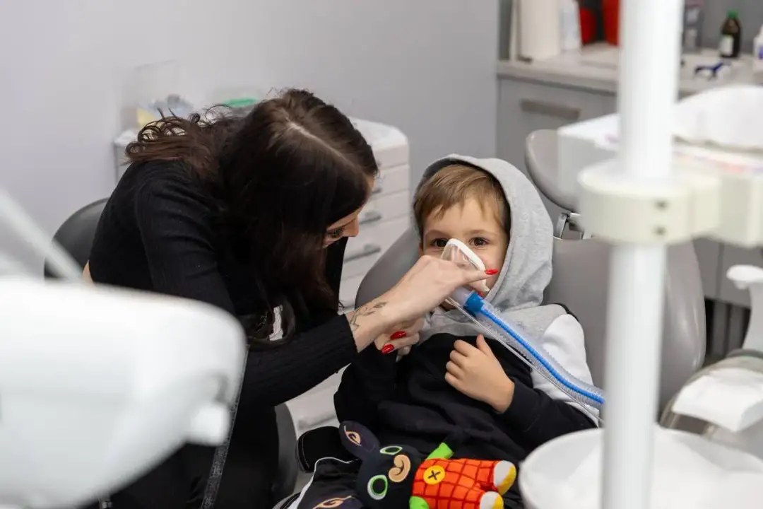 Dziecko w masce znieczulającej u dentysty, trzymanej przez kobietę.