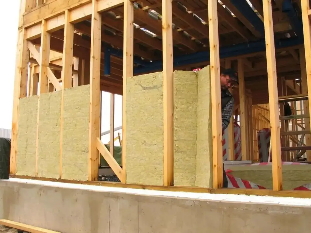 Budowa domu: montaż wełny mineralnej w drewnianej konstrukcji ścian.