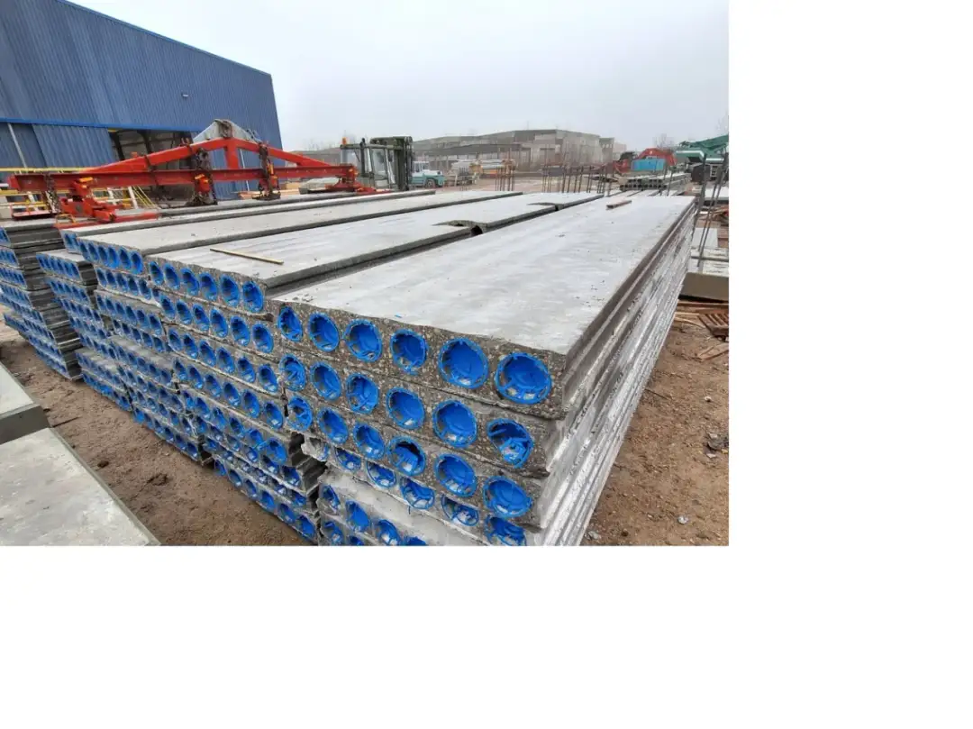 Stos płyt kanałowych z niebieskimi otworami na placu budowy.