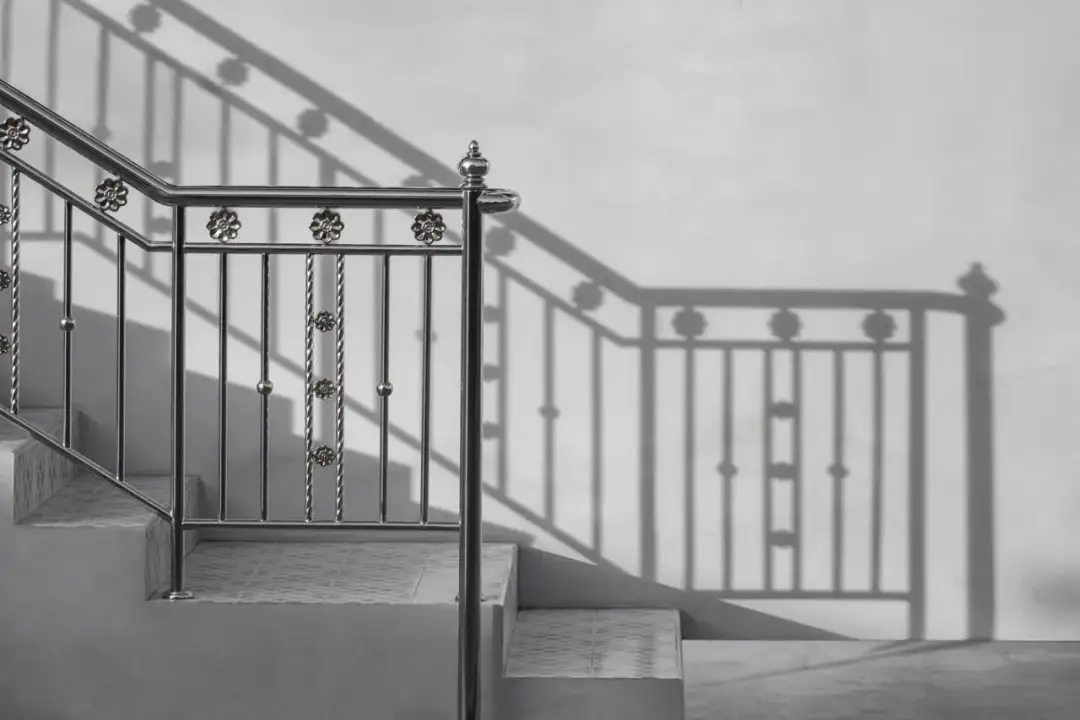 Metalowa balustrada schodowa z ozdobnymi elementami i jej cień na ścianie.