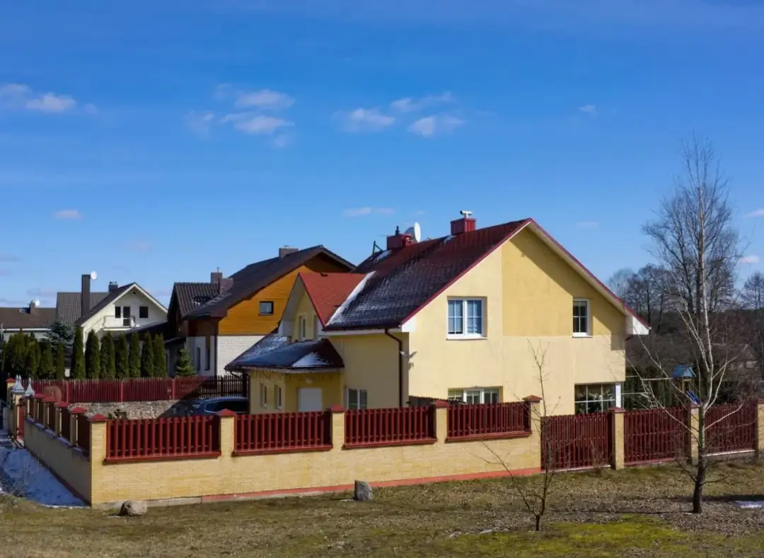 Domy jednorodzinne z czerwonymi dachami i żółtymi elewacjami, ogrodzone płotem.