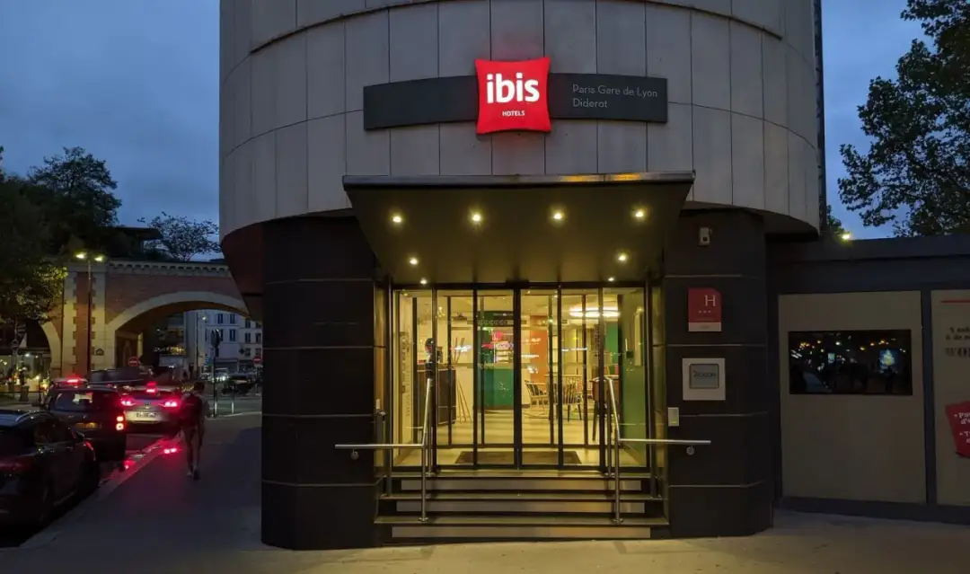 Wejście do Ibis Hotel Paris Gare de Lyon Diderot nocą. Widać podświetlany znak hotelu, szklane drzwi i schody.