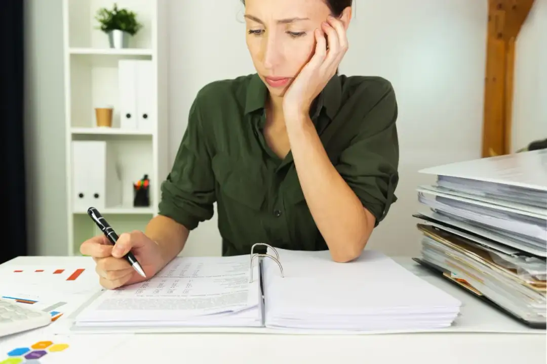 Kobieta w zielonej koszuli pochyla się nad dokumentami, trzymając długopis.