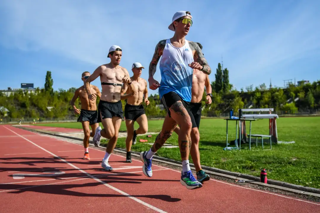 Biegacze na bieżni stadionu, która ma 400 metrów. Słońce świeci, a zawodnicy w skupieniu pokonują kolejne metry.