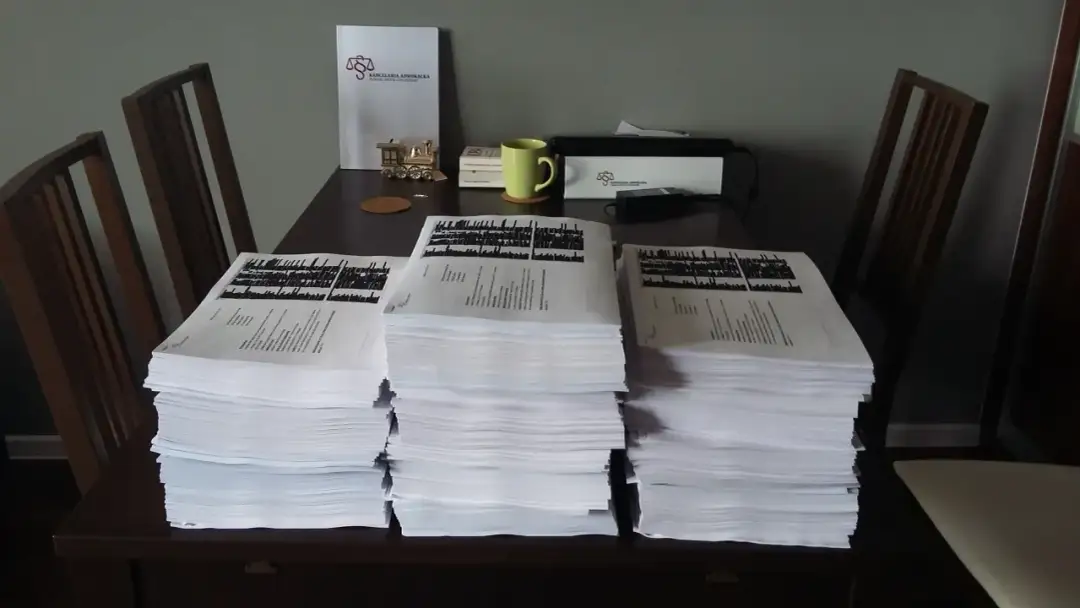Stosy dokumentów na stole, obok nich dokument kancelarii adwokackiej. Gdy potrzebujesz pomocy, gdzie złożyć skargę na wspólnotę mieszkaniową, warto udać się do prawnika.