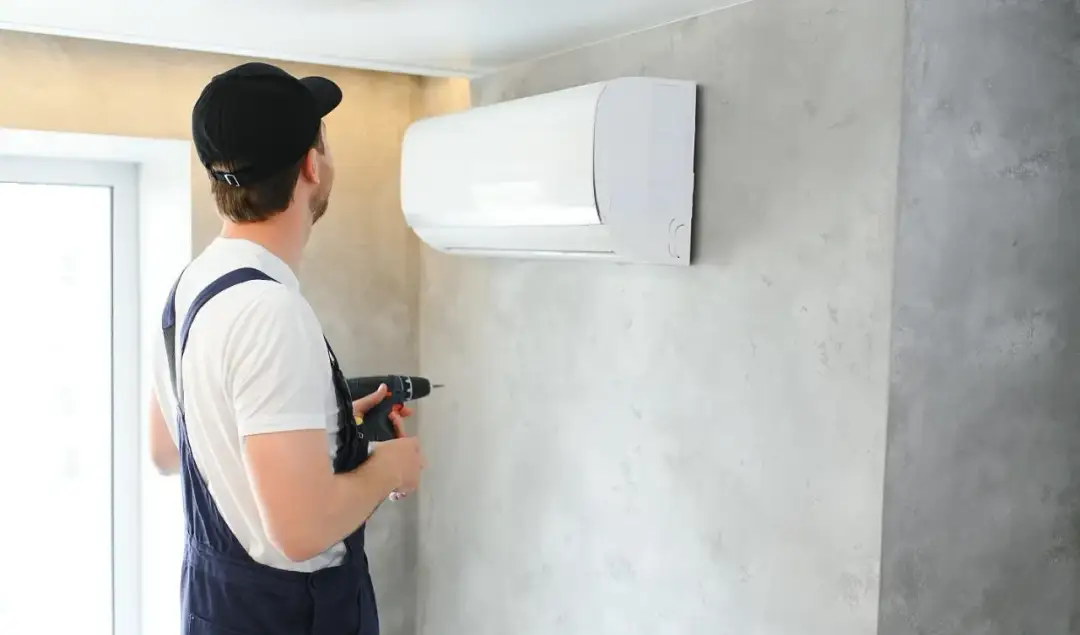 Instalator z wiertarką przy klimatyzatorze. Kluczowe jest, jak dobrać średnice rur do klimatyzacji, by zapewnić jej efektywność.